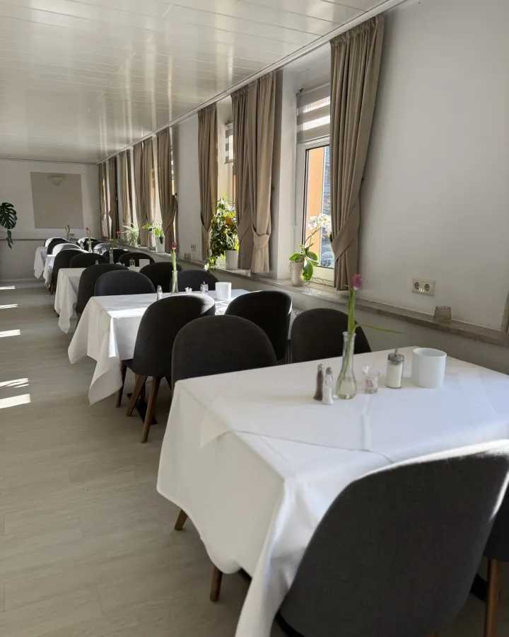 Frühstücksraum mit weiß gedeckten Tischen und hellen Fenstern